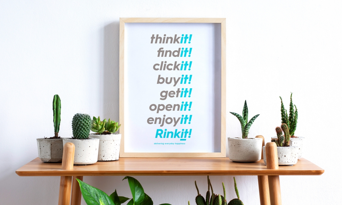 A wooden table surrounded by indoor plants with a frame on the table showing Rinkits 'it' language