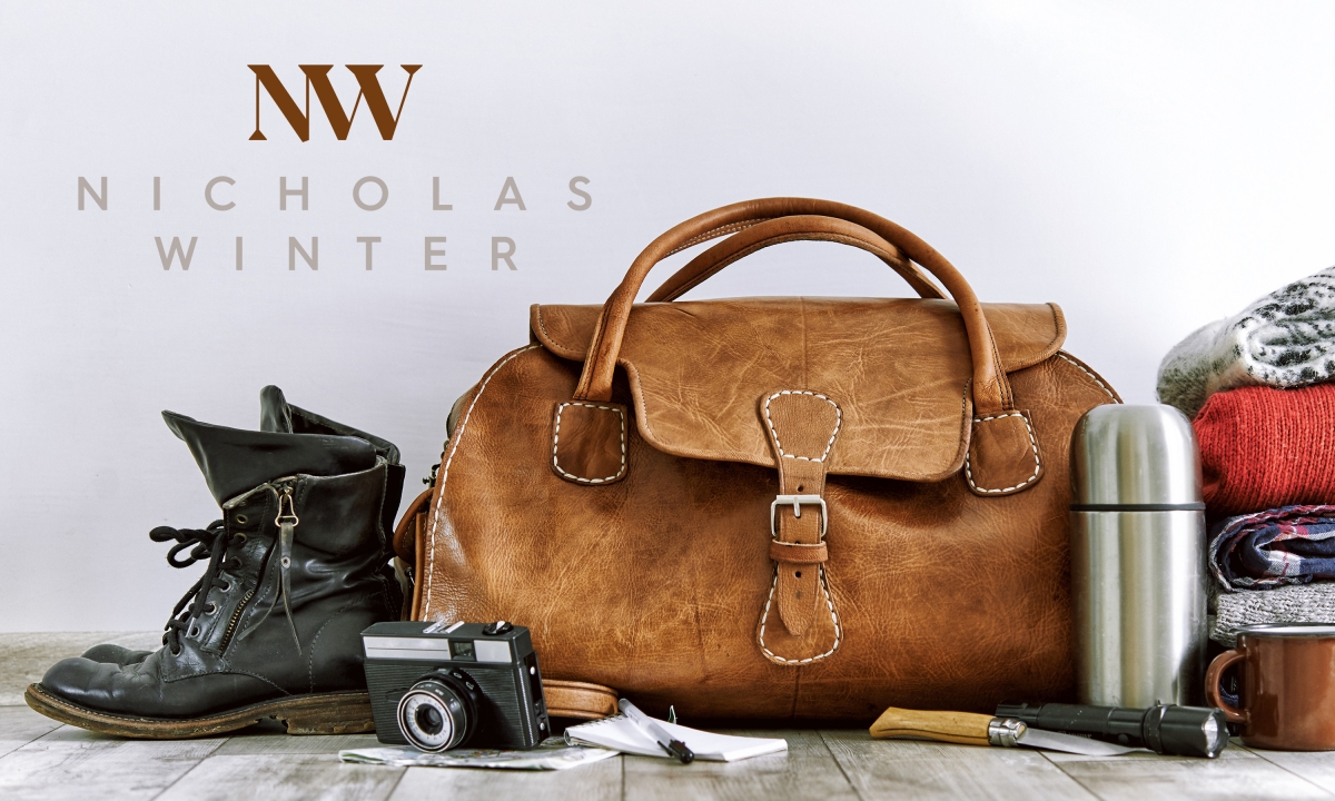 An old leather bag and camera with walking boots featuring a Nicholas Spring brand mark